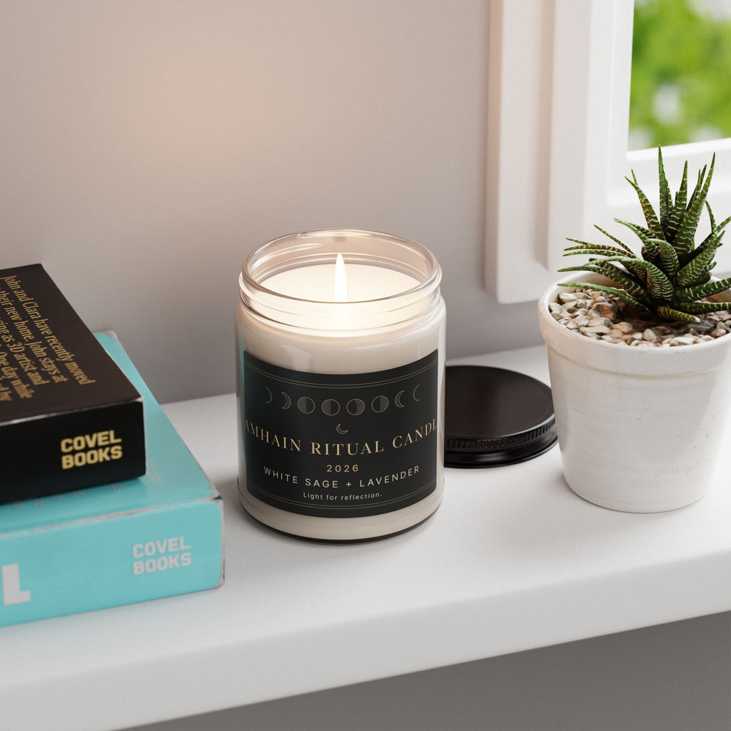 Lit White Sage and Lavender Samhain Ritual Candle on a desk beside books and a potted succulent
